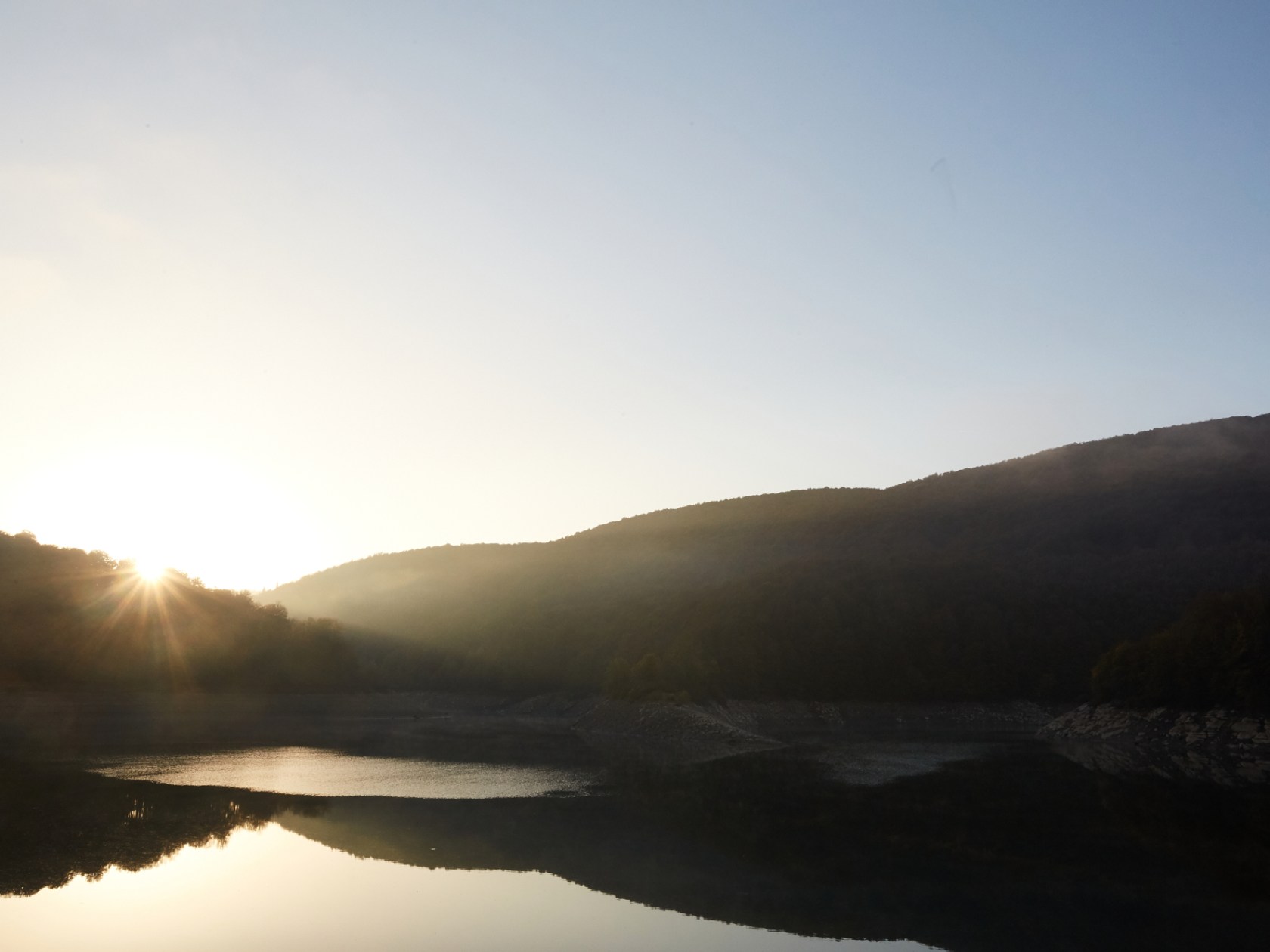 a sunset over a body of water with a mountain in the background