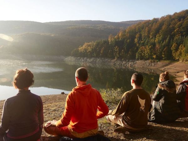 Grupo de personas sentadas frente al lago en retiro de yoga y meditación en Pirineos