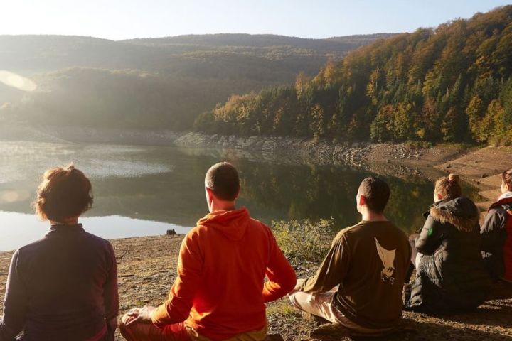 Grupo de personas sentadas frente al lago en retiro de yoga y meditación en Pirineos